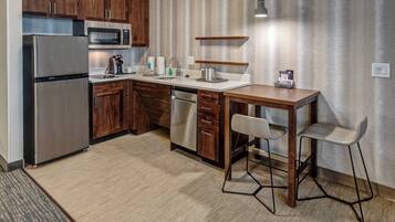 A modern kitchen with wooden cabinets, stainless steel appliances, a built-in microwave, a coffee maker, and a small dining area with stools.
