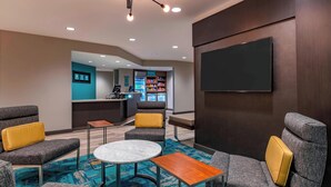 Ein moderner Lounge-Bereich mit grauen gepolsterten Sofas, einem runden Marmortisch und einem an der Wand montierten Flachbildfernseher.