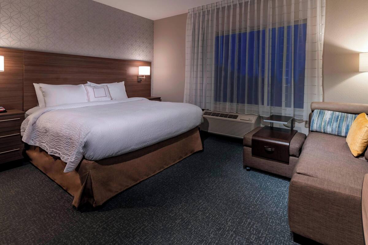 A hotel room with a large bed, a sofa, a desk, and a window with curtains.