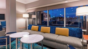 Eine Hotellobby mit einer Couch, zwei runden Tischen und einem großen Fenster mit Blick auf die Stadtlandschaft.