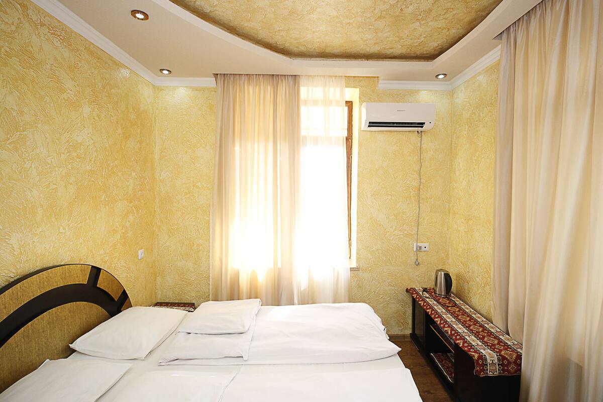 Une chambre d’hôtel équipée d’un lit, d’une table de chevet, d’un appareil de climatisation et d’une fenêtre avec des rideaux.