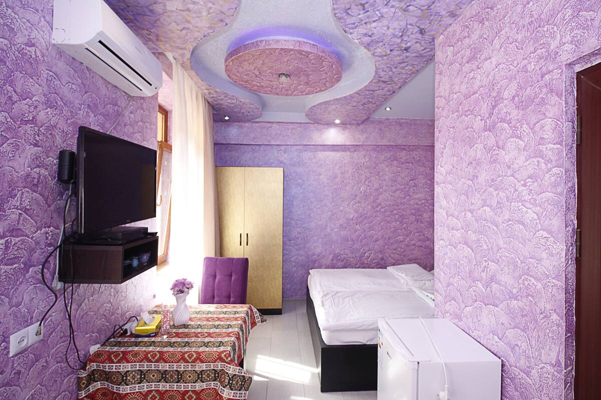 Une chambre à coucher avec un lit, une télévision, une armoire et une petite table sur laquelle se trouve un vase.