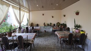 A restaurant with multiple tables and chairs, potted plants on the walls, and a view of a garden through the windows. - Planet Yerevan Hotel (Yerevan)