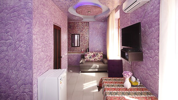 A room with purple patterned walls, a sofa, a TV, and a bed with patterned bedding. - Planet Yerevan Hotel (Yerevan)