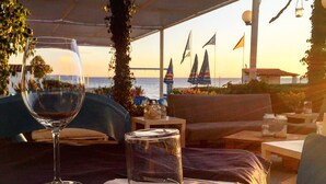 A table set for two with a glass of wine, a glass of water, and cutlery. The setting appears to be outdoors with a view of the sea and flags in the background. - Residence le 4 stagioni (Menfi)
