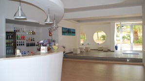 A modern reception area with a bar, shelves of bottles, and a view of the outdoors through large windows. - Residence le 4 stagioni (Menfi)