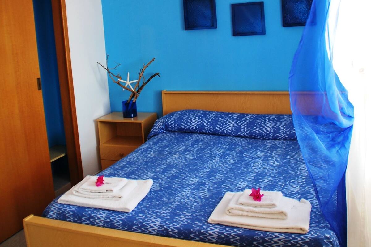 A bedroom with a wooden bed, blue walls, and a small bedside table with a vase.