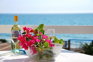 A table with a glass bowl of flowers and a wine bottle, set against a view of the sea. - Residence le 4 stagioni (Menfi)