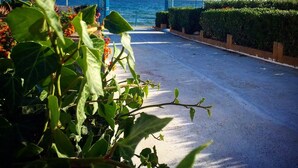 A coastal road with a blue archway leading to the sea, flags on poles, and greenery in the foreground. - Residence le 4 stagioni (Menfi)