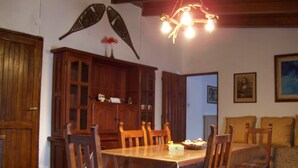 A dining area with a wooden table, chairs, and a chandelier. There is a wooden cabinet with glass doors and a vase with flowers on the table.