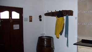 A room with a wooden door, a large barrel, a coat rack with jackets, and a small cabinet.
