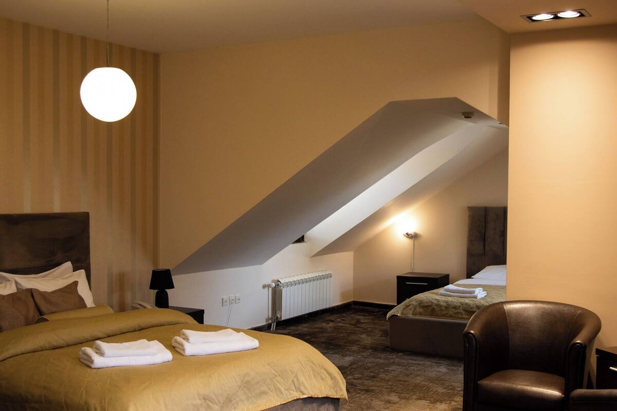 A bedroom with a bed, a chair, a radiator, and a sloped ceiling.
