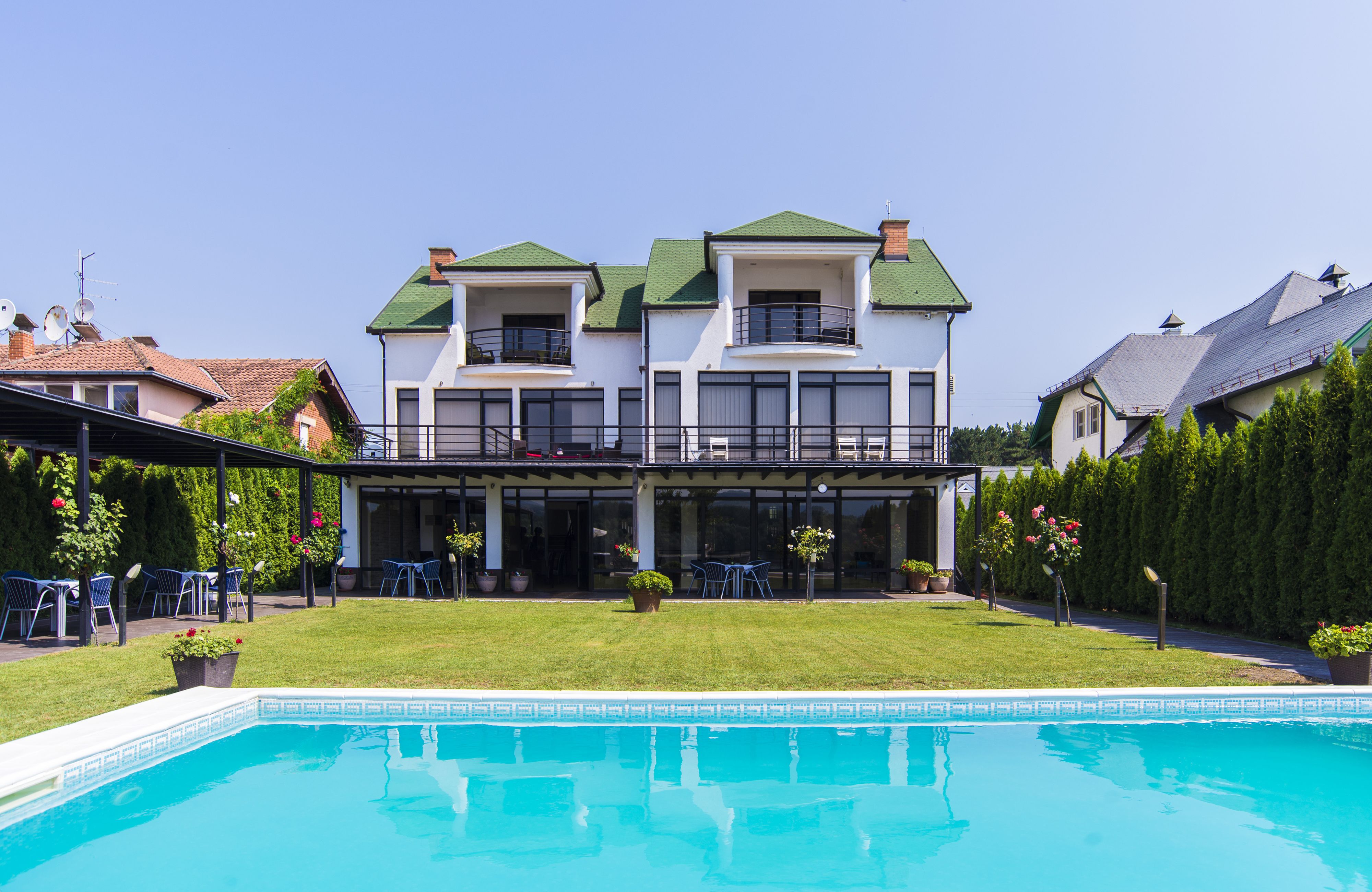 A two-story house with a pool, a covered patio, and a well-maintained lawn.