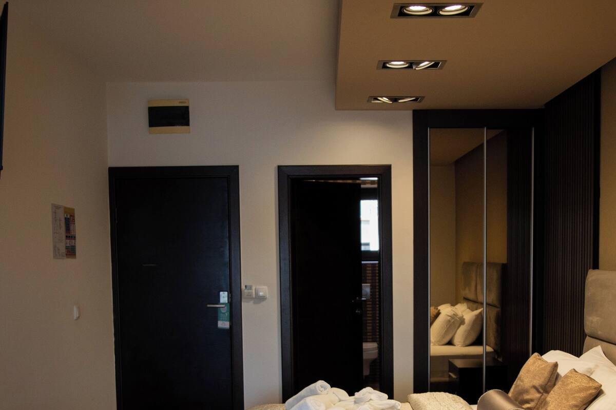 A hotel room with a bed, a desk, a chair, a mirror, and a door.