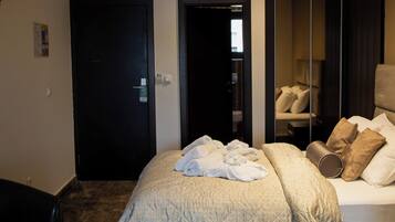 A hotel room with a bed, a desk, a chair, a mirror, and a door.