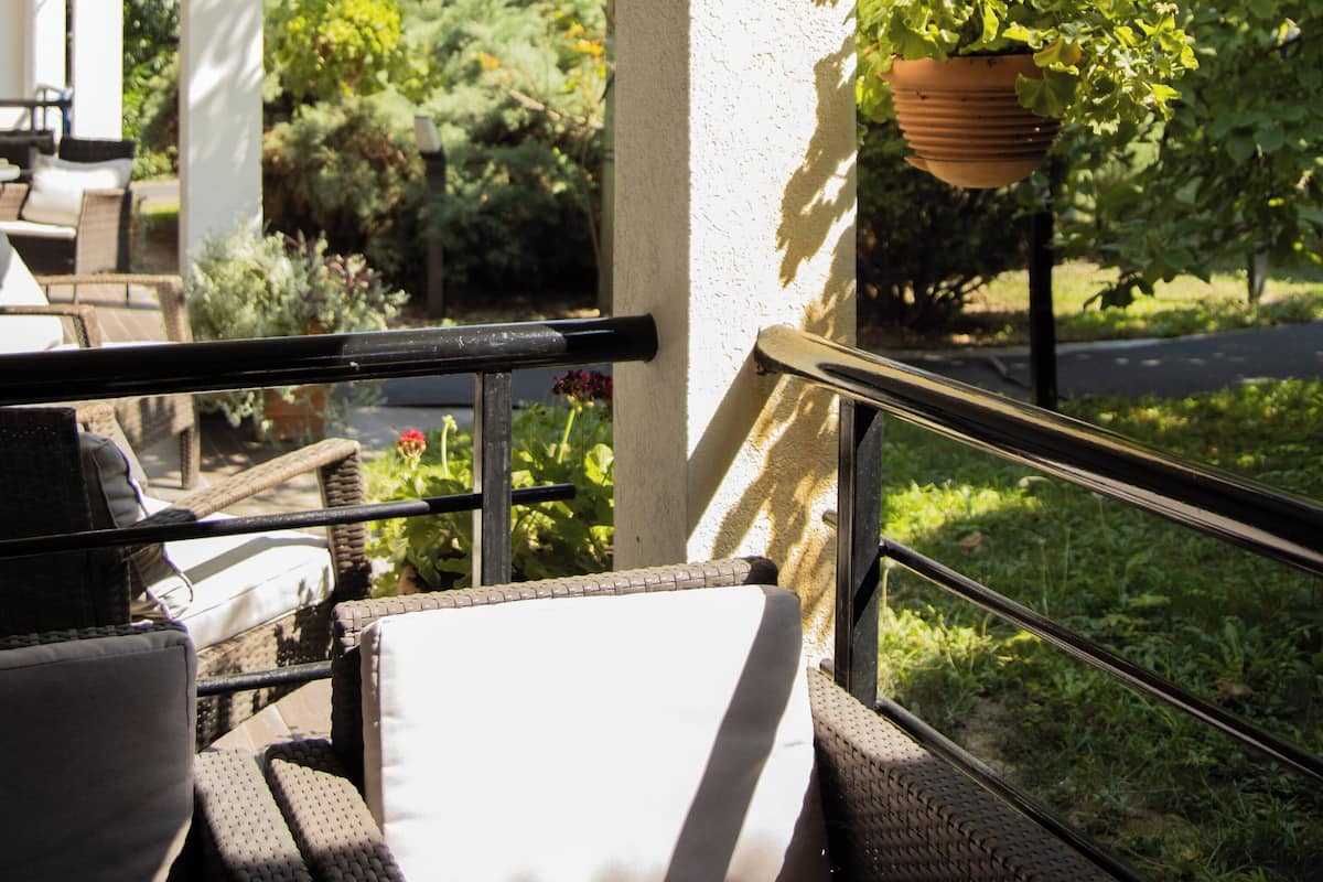 An outdoor patio with a seating area, a hanging flower pot, and a view of greenery and a road.