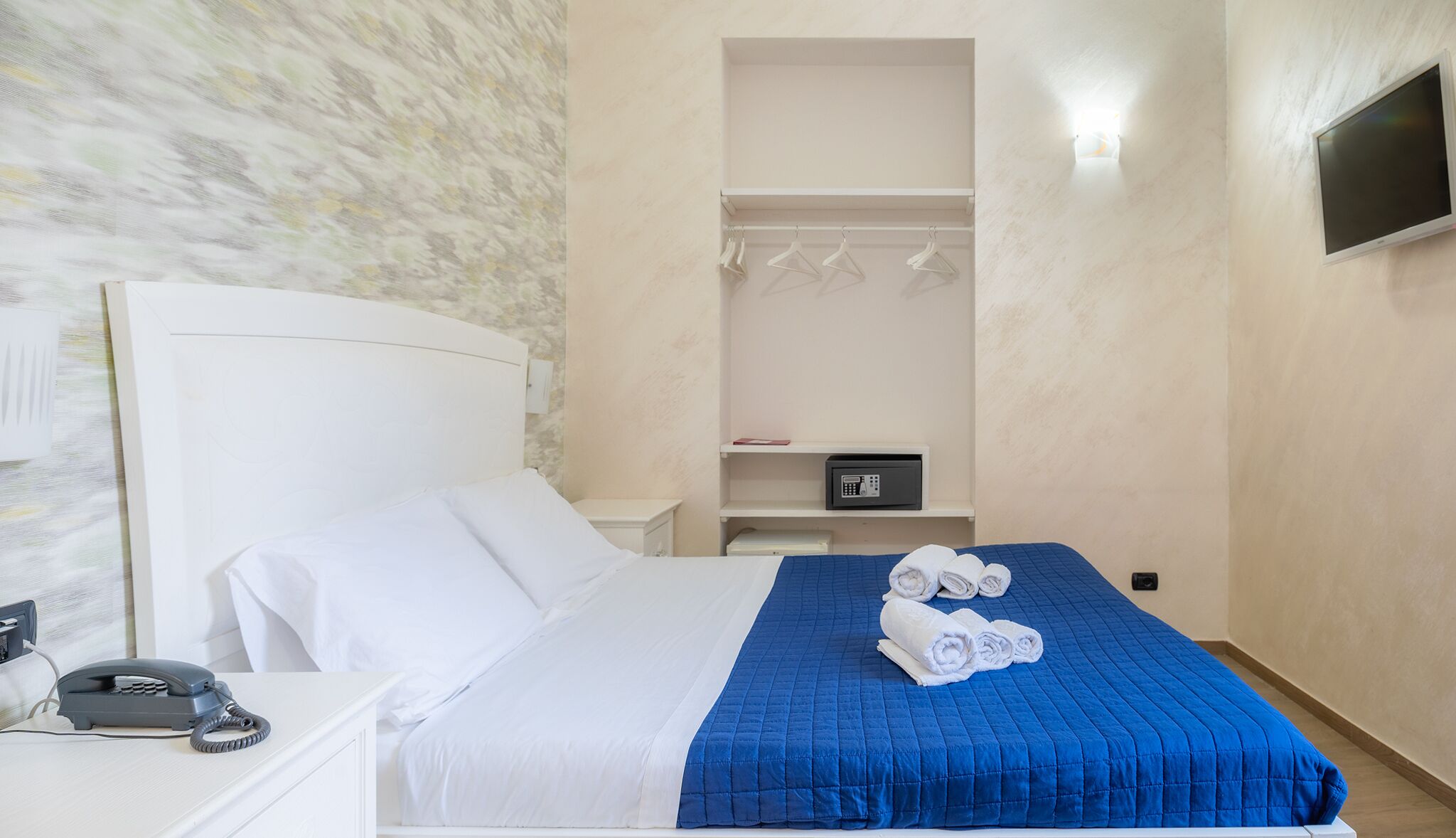 Ein Hotelzimmer mit Bett, Nachttischtelefon, Mikrowelle und einem an der Wand montierten Fernseher.