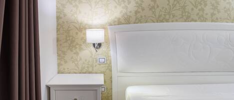 A hotel room with a bed, nightstand, lamp, and floral wallpaper.