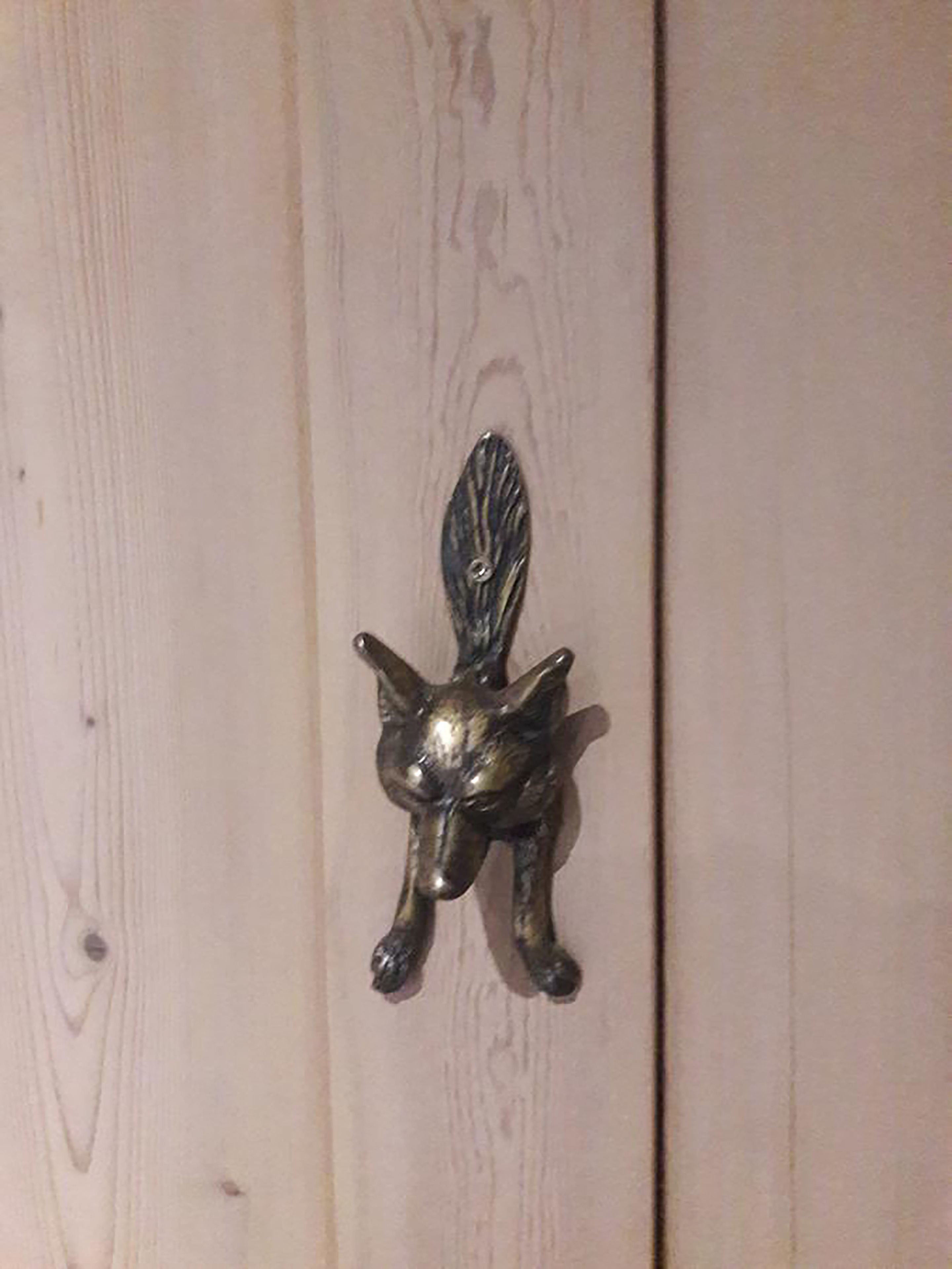 A metallic cat-shaped door knocker on a wooden door.