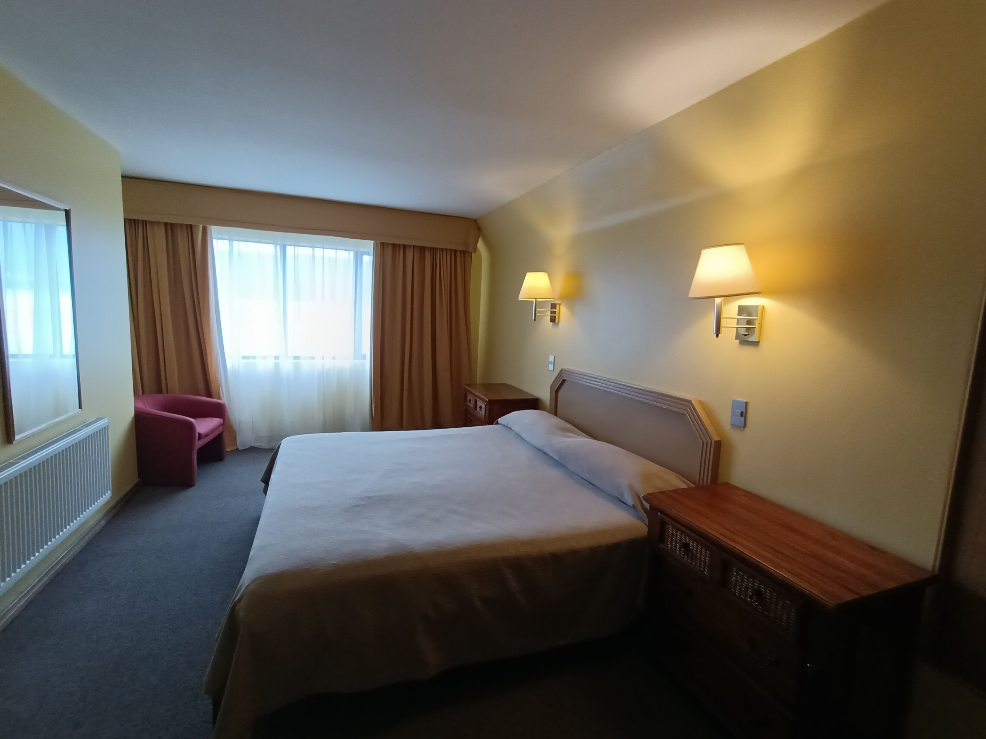 A hotel room with a large bed, two bedside tables, a chair, and a window with curtains.