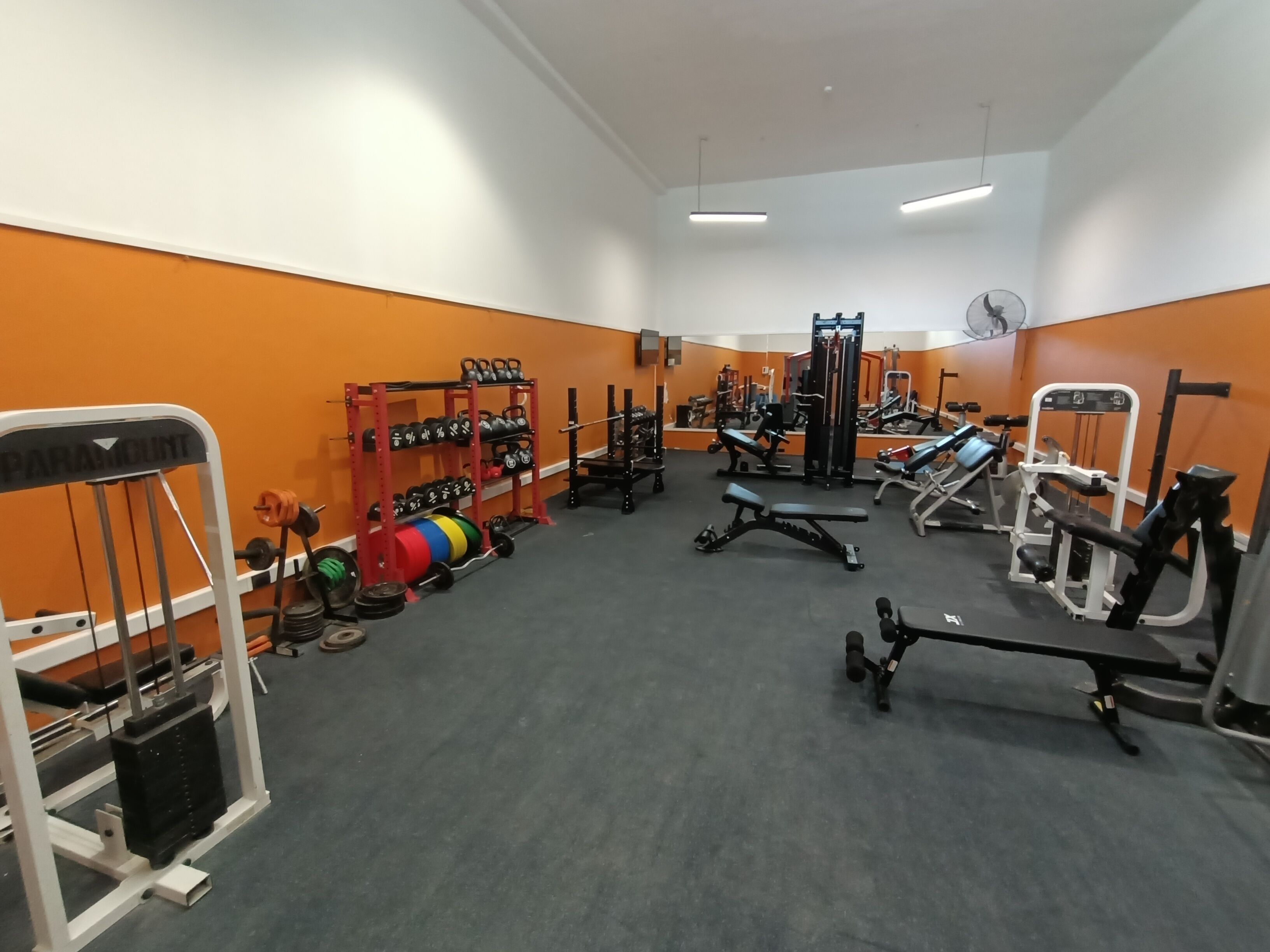 Een sportschool met diverse fitnessapparaten, waaronder krachttoestellen, banken en losse gewichten.