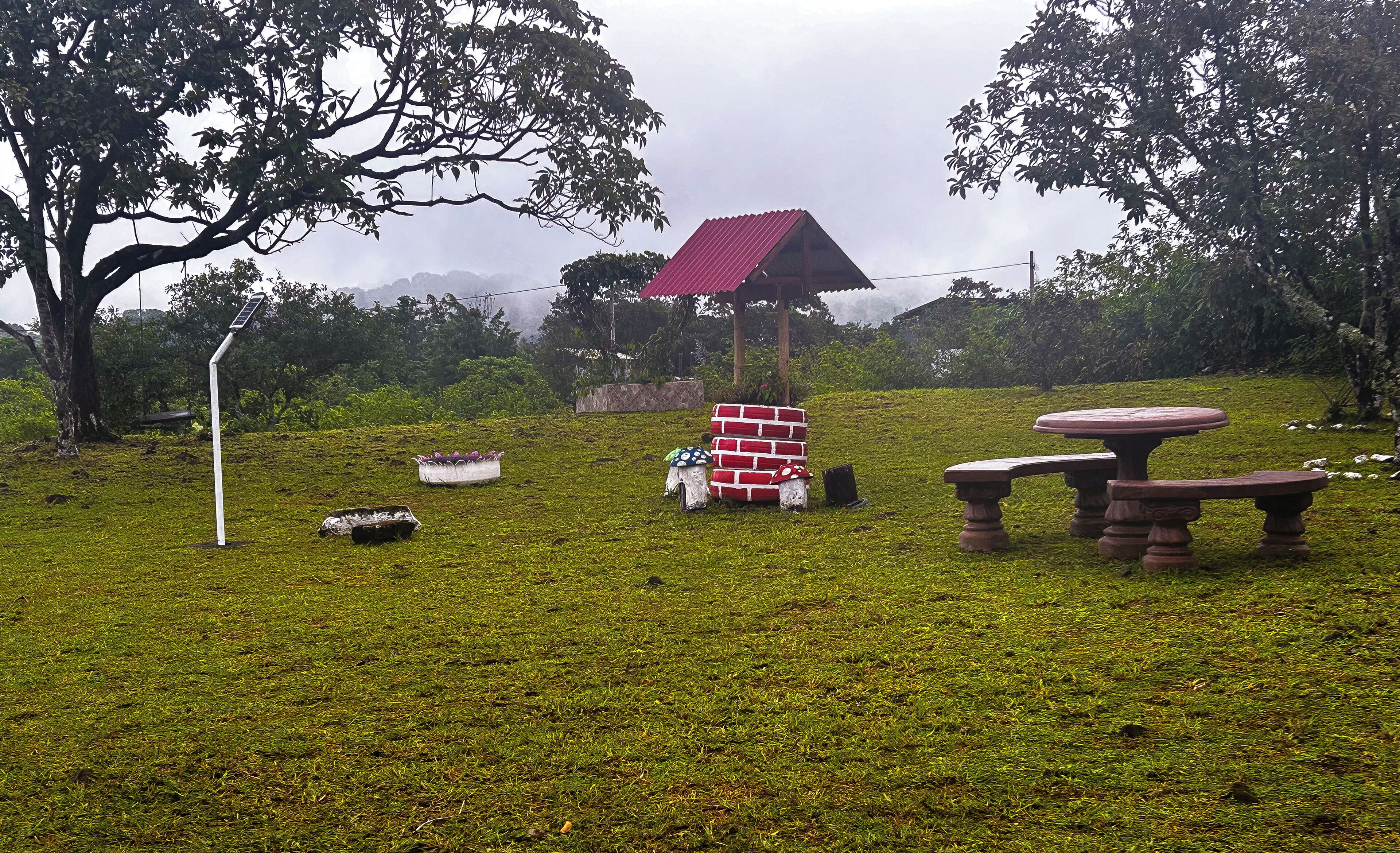 A grassy area with a red-roofed pavilion, a white bench, and a table.