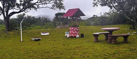 A grassy area with a red-roofed pavilion, a white bench, and a table.