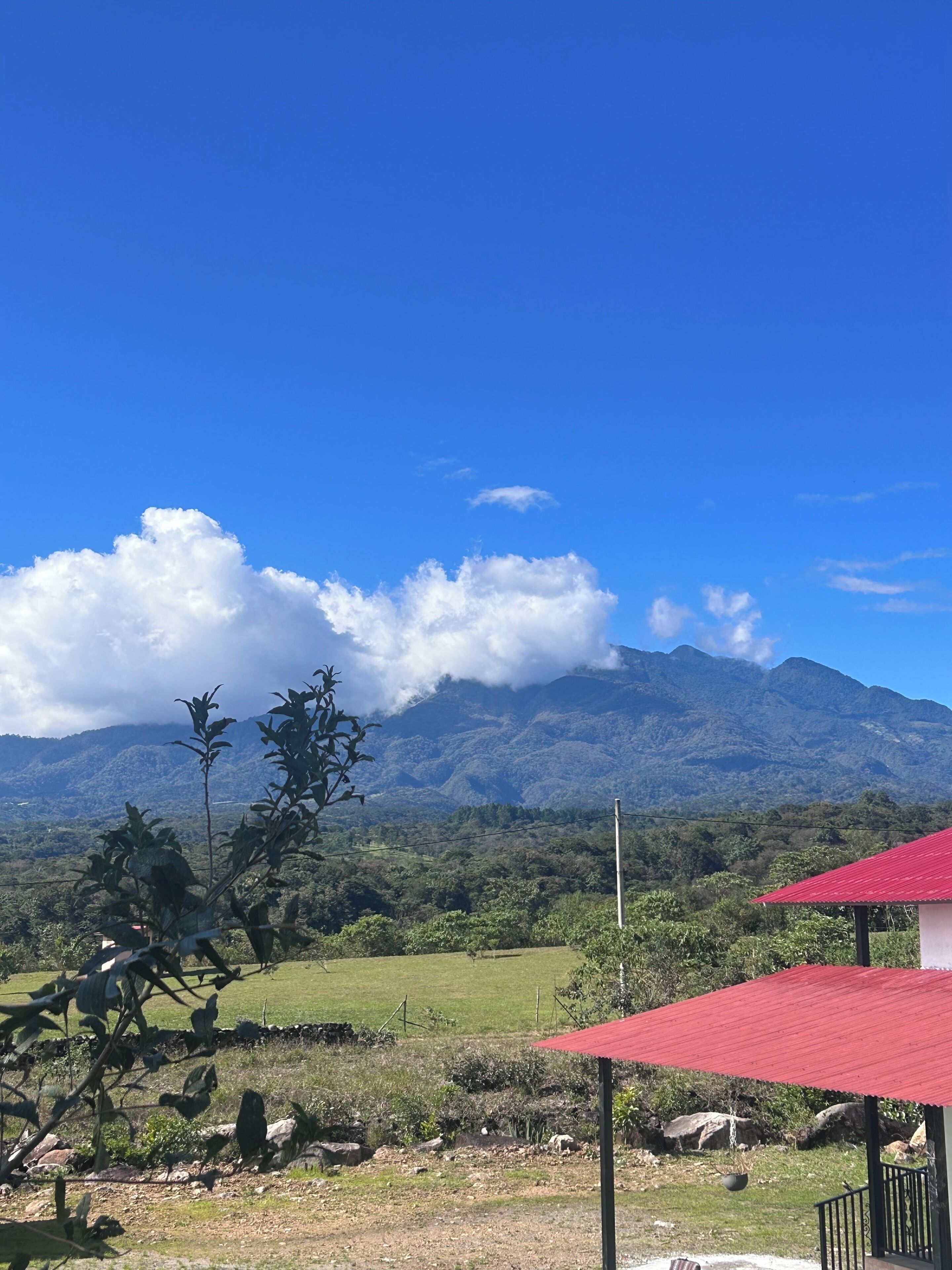 A mountainous landscape with a clear sky, a red-roofed structure, and lush greenery.