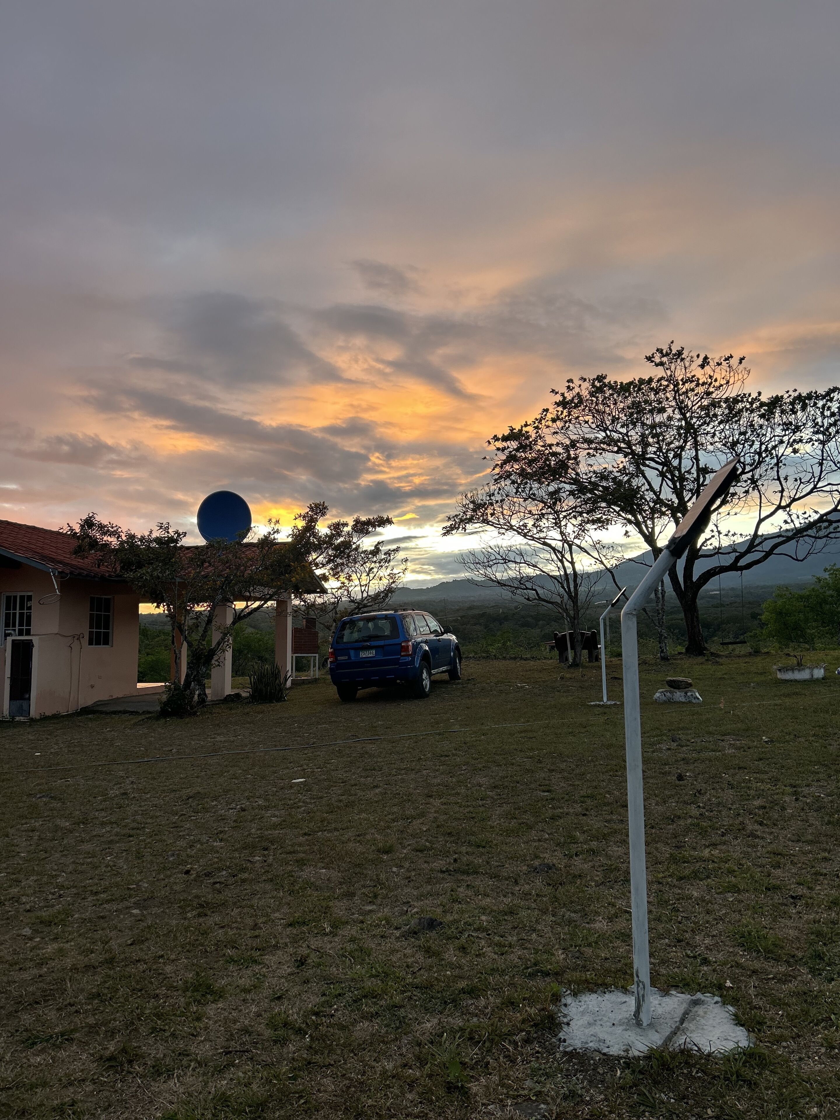 Une maison avec une voiture garée dans l’allée, un arbre et un ciel dégagé.