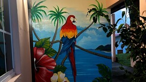 Un pasillo con un mural de un loro en una rama, palmeras y flores.