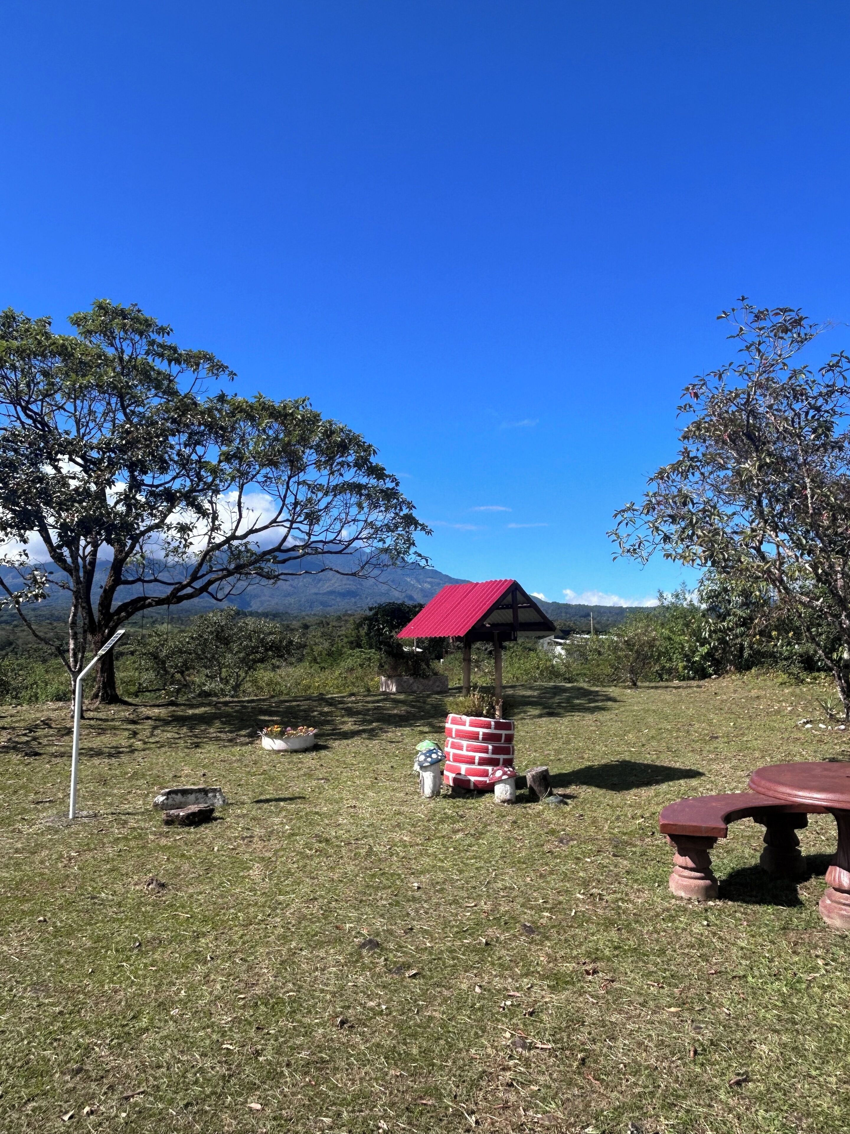A picnic area with a red-roofed shelter, a picnic table, and a stone bench.