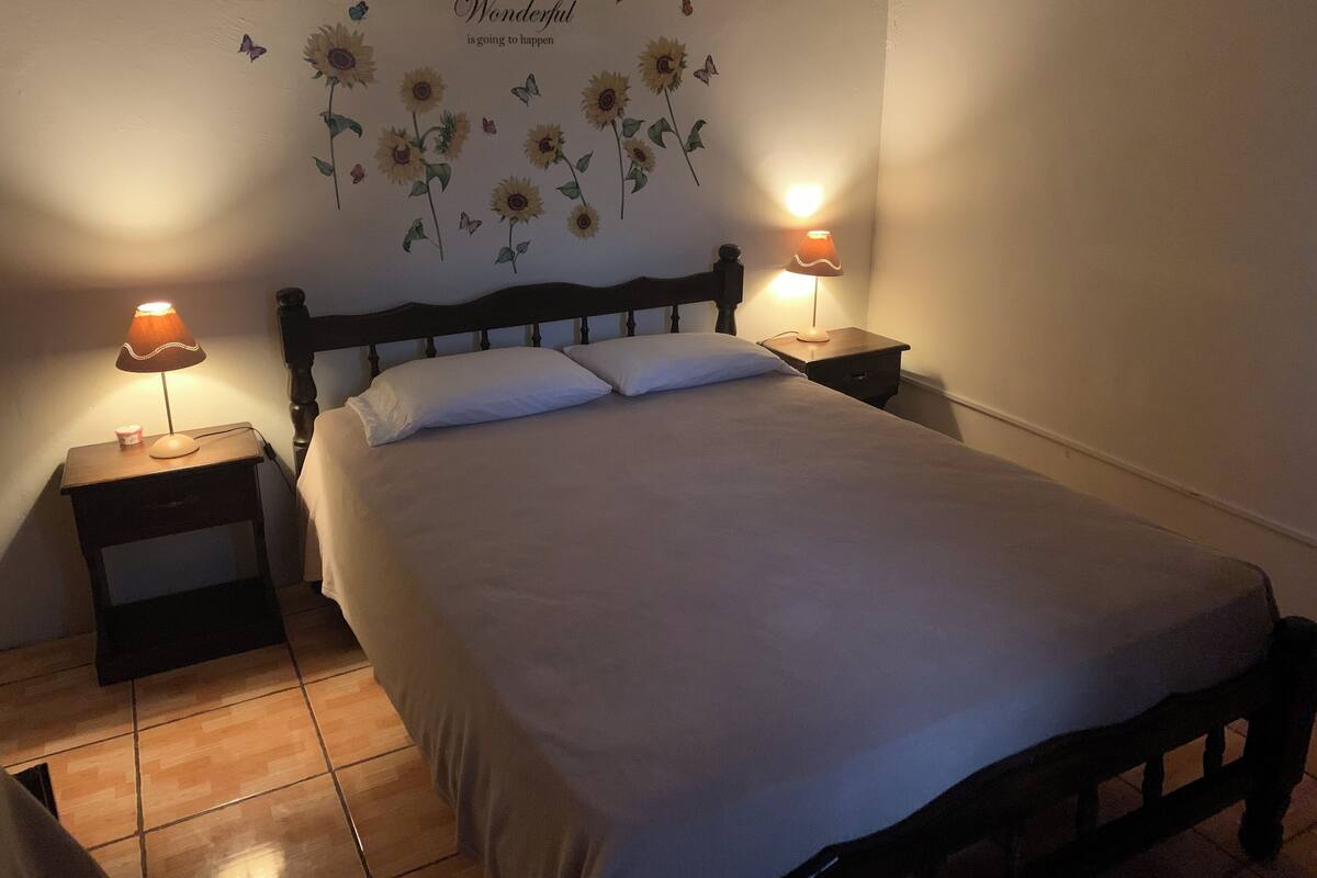 Una cama bien tendida con dos almohadas, un cabecero de madera y dos mesitas de noche con lámparas.