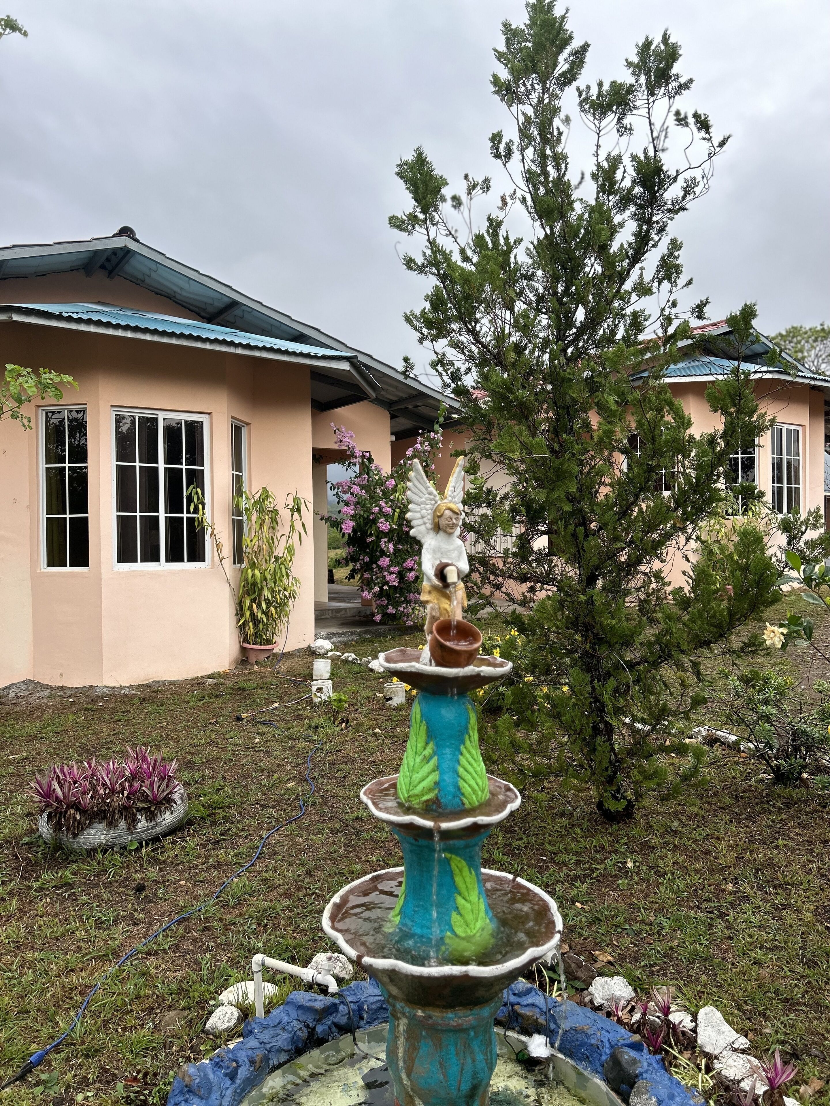 A house with a garden, a fountain with an angel statue, and a tree.