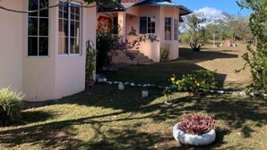 Una casa de un piso con techo de tejas rojas, un porche cubierto y un césped bien cuidado.