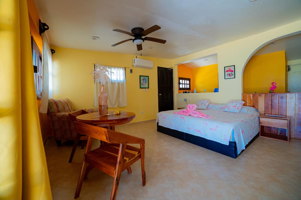 A hotel room with a bed, a desk, a chair, a ceiling fan, and a bathroom visible through an archway.