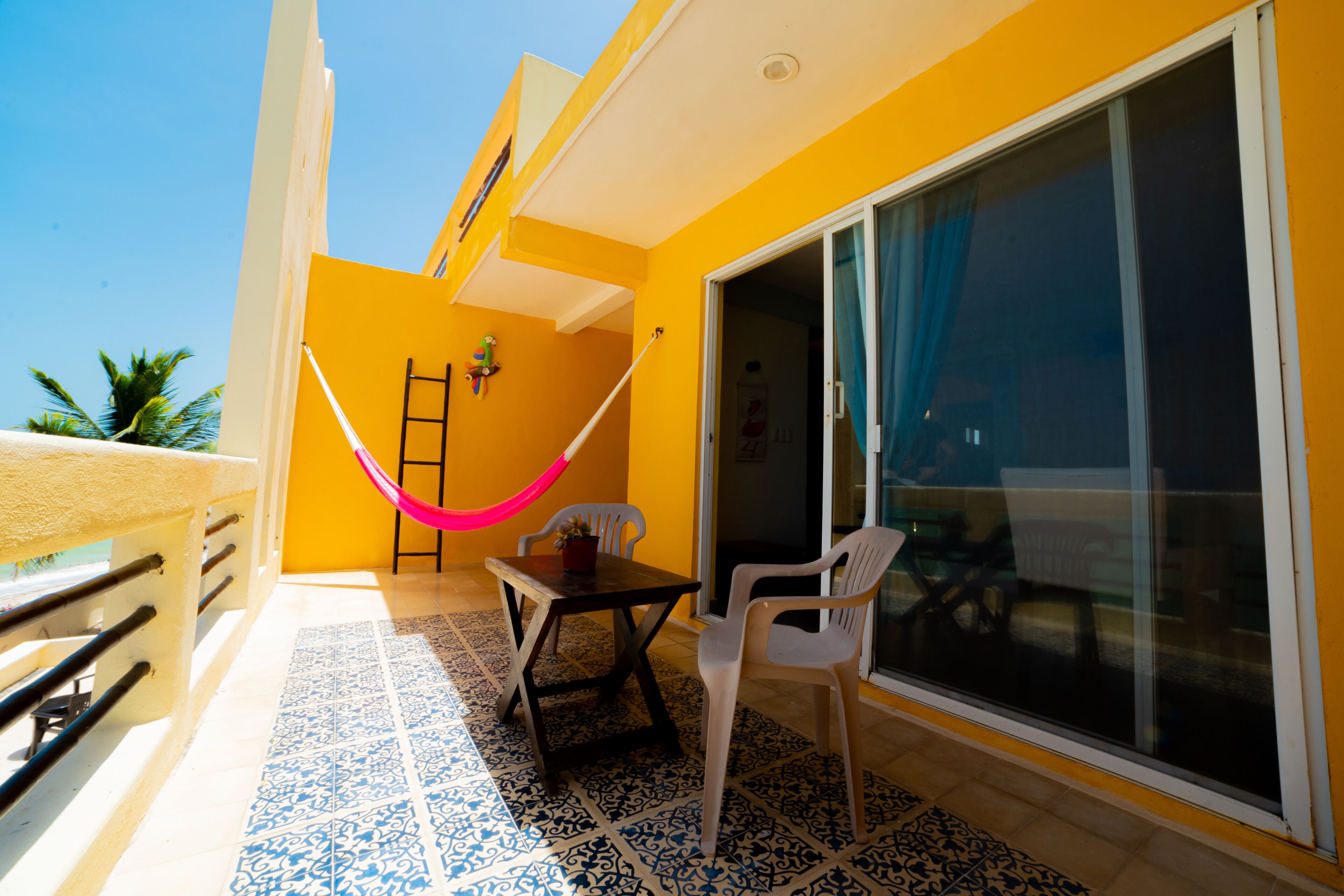 A balcony with a hammock, a table, chairs, and a large sliding glass door.