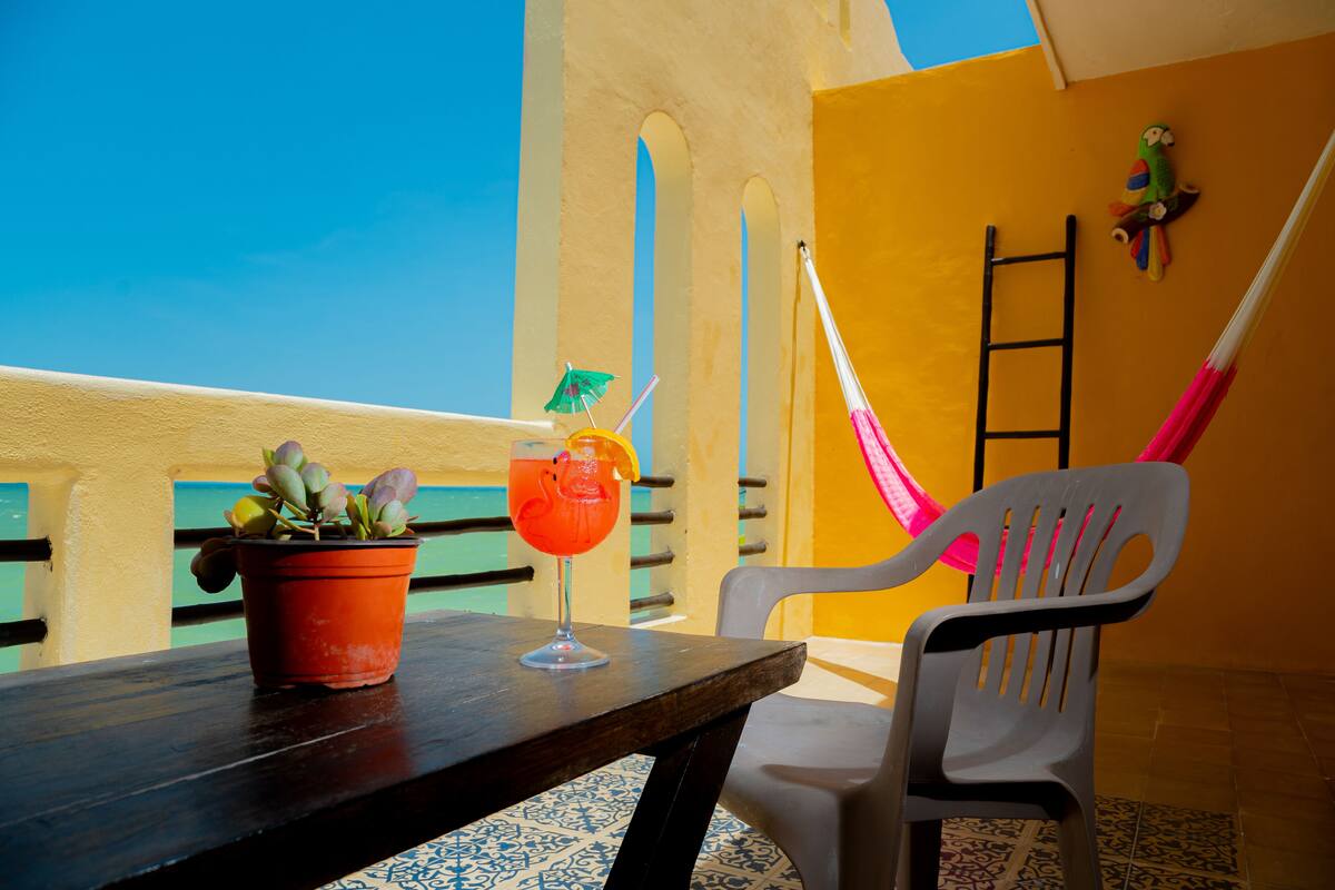 A balcony with a table, a potted plant, a cocktail, and a plastic chair.