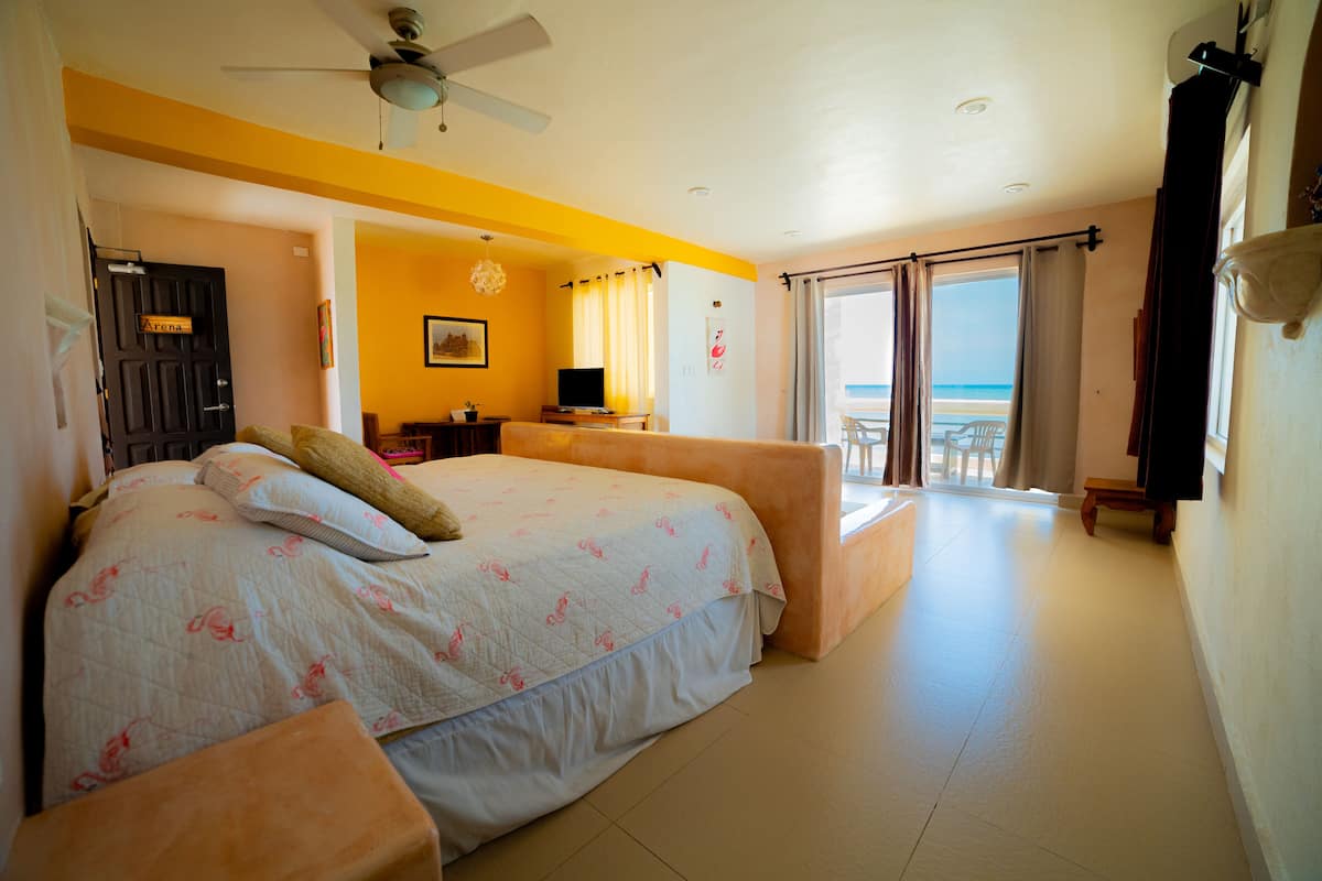 A bedroom with a bed, a desk, a chair, and a view of the beach.