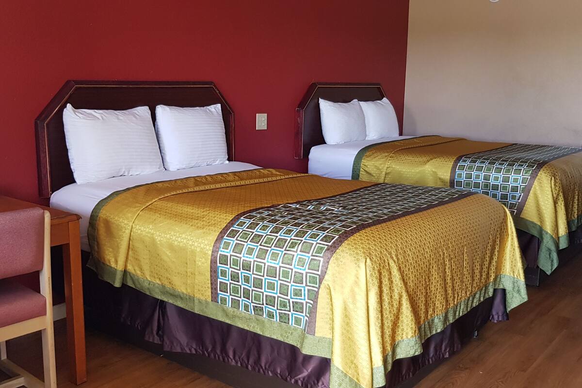 A hotel room with two beds, each with a patterned bedspread, a wooden nightstand with a tissue box, and a chair.