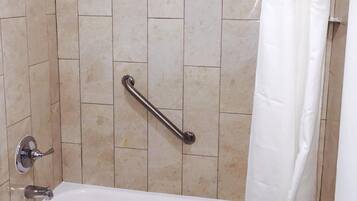 A bathroom with a bathtub, a shower, and a handrail.