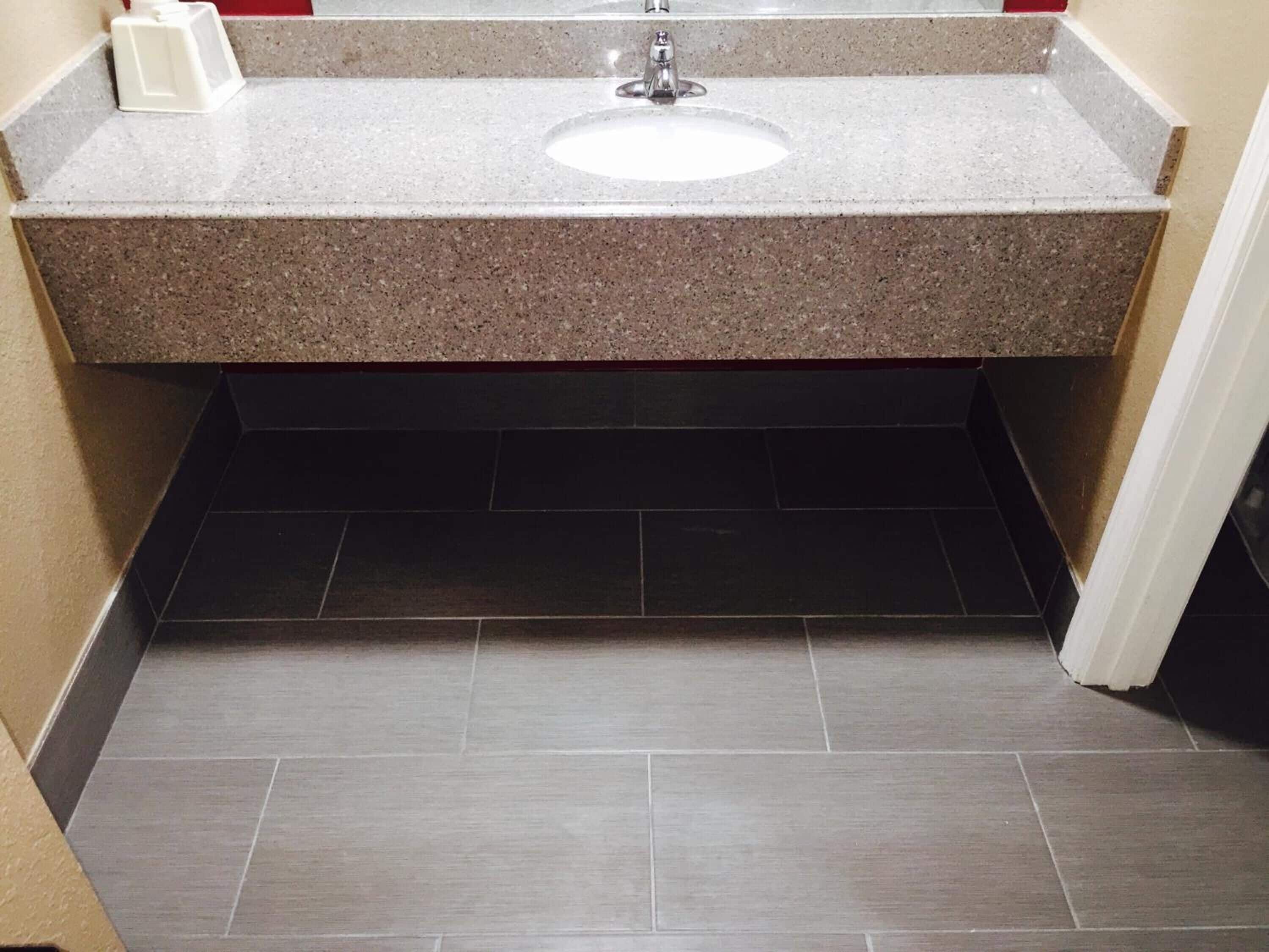 A bathroom with a granite countertop, a white sink, and dark tiled flooring.
