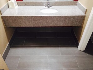A bathroom with a granite countertop, a white sink, and dark tiled flooring. - Deluxe Inn (West Memphis)
