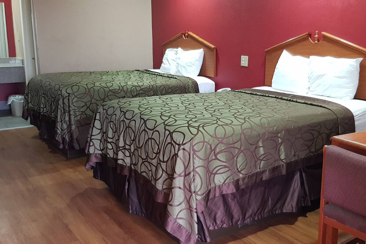 A hotel room with two beds, a wooden desk, and a chair.