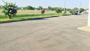 A parking lot with a truck and a trailer, surrounded by greenery and a clear sky. - Deluxe Inn (West Memphis)