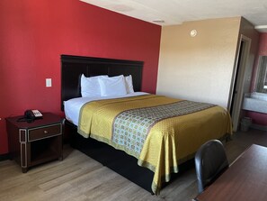 A hotel room with a bed, a nightstand, a desk, and a chair. - Deluxe Inn (West Memphis)