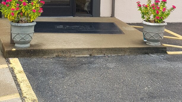 The exterior of a hotel named 'Deluxe Inn' with a prominent sign, a glass entrance, and two potted plants. - Deluxe Inn (West Memphis)