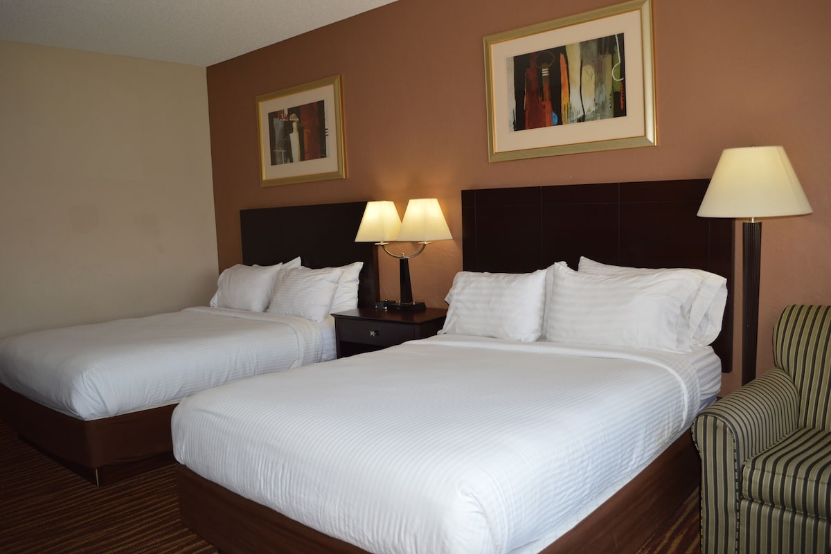 A hotel room with two beds, a nightstand, a lamp, and two framed pictures on the wall.