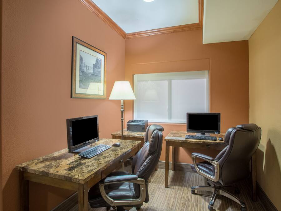 A hotel room with two desks, each with a computer and a lamp, leather chairs, and a framed picture on the wall.