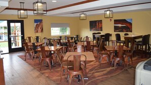 A dining area with multiple tables and chairs, wooden beams on the ceiling, and artwork on the walls.