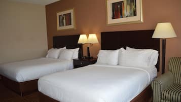 A hotel room with two beds, a nightstand with lamps, a chair, and two framed pictures on the wall.